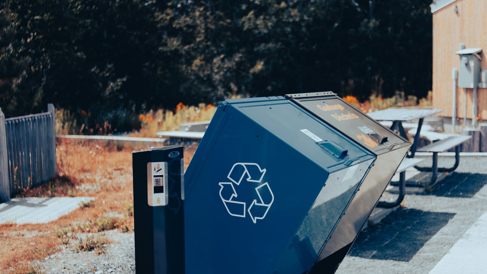 Blauwe afvalcontainer met recyclelogo bij een milieustraat op een zonnige dag
