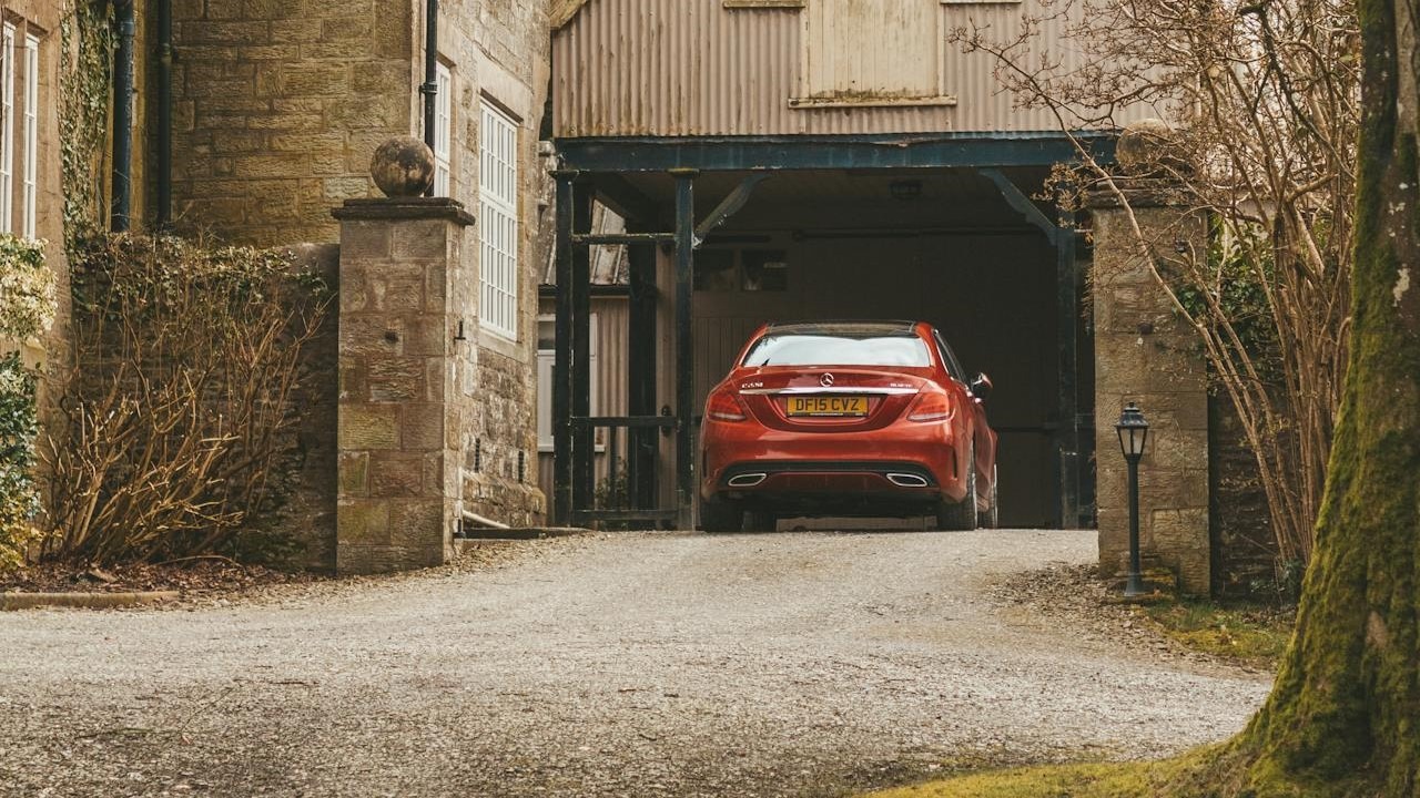 Rode auto geparkeerd op een grindoprit bij een landelijke stenen woning met carport