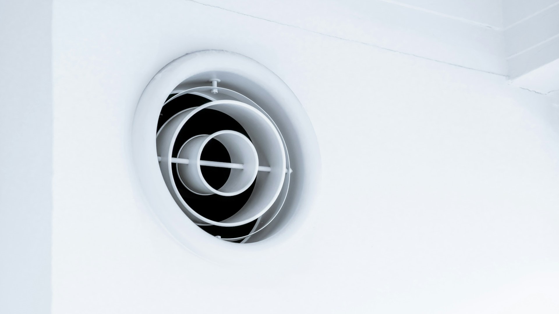 Ventilatierooster aan plafond met ronde lamellen voor luchtcirculatie in een wit interieur