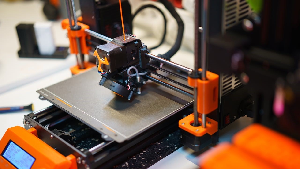 FDM 3D-printer in actie met oranje accenten en printkop die filament extrudeert op verwarmd printbed