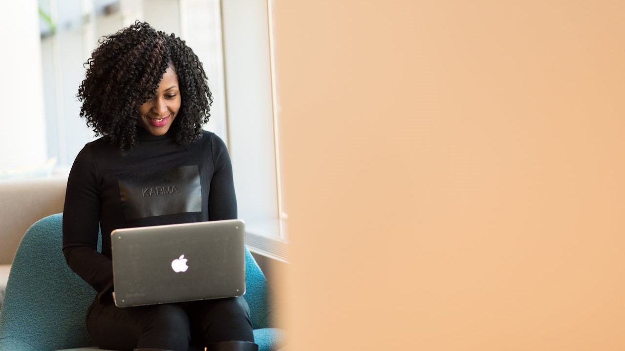Vrouw werkt glimlachend op een laptop in moderne kantooromgeving, mogelijk bezig met kennisoverdracht of inwerkproces