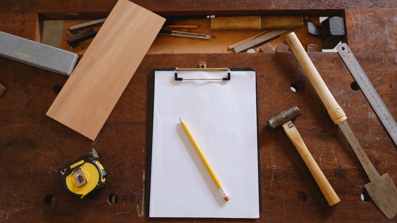Startkosten timmerman inzichtelijk maken met lijst op clipboard tussen gereedschap op houten werkbank