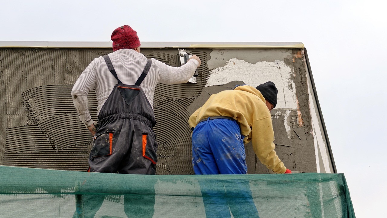 Twee stucadoors brengen buiten stucwerk aan op een gevel, wat invloed heeft op het uurtarief stucadoor.