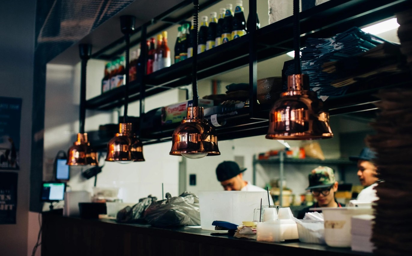 Drukke horecakeuken met koks aan het werk, industriële verlichting en voorraad op open schappen
