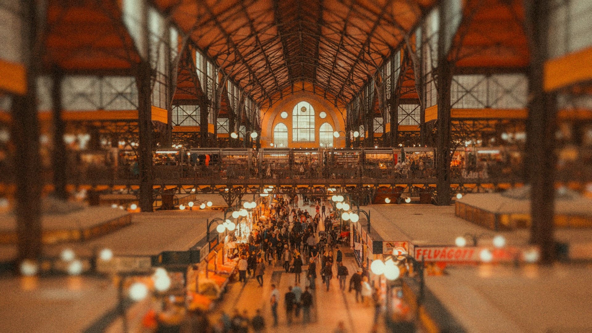 Overzicht van een grote overdekte markthal vol bezoekers en verlichte stands