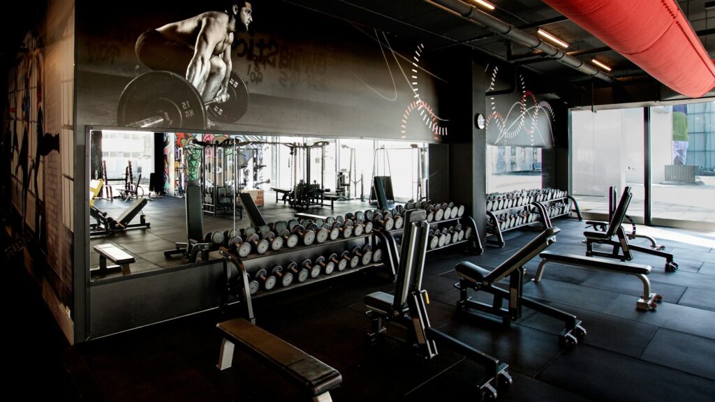 Moderne fitnessruimte met halters, banken en spiegels, relevant voor onderhoudskosten fitnessapparatuur