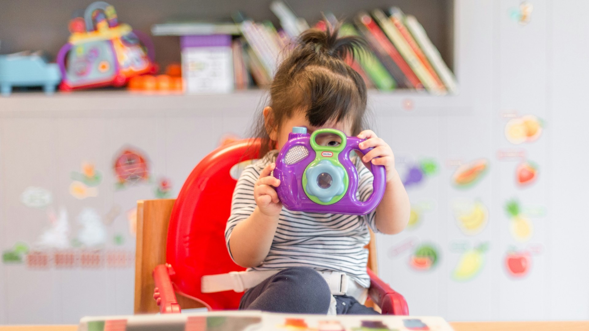 kinderopvang aan huis met peuter die speelt met speelgoedcamera in kindvriendelijke speelruimte