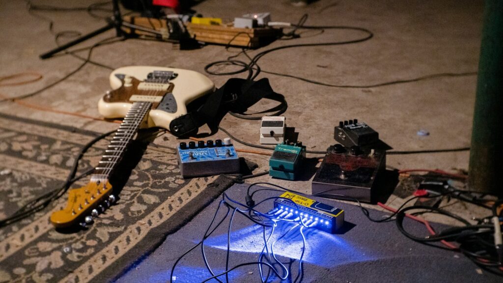 Elektrische gitaar set met effectpedalen en kabels op vloer tijdens oefensessie